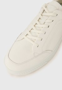 Weiße Sneakers mit einem strukturierten Lederoberteil, flachen Schnürsenkeln, runder Zehenpartie und einer Gummisohle mit einem dezenten Profilmuster.