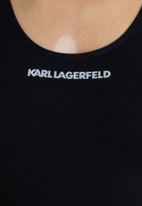 Černý top bez rukávů s kulatým výstřihem a bílým logem "KARL LAGERFELD" na hrudi, vyrobený z měkké a elastické látky.