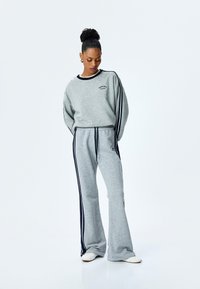 Grijze sweatshirt en bijpassende broek met marineblauwe zijstrepen. Zacht materiaal, losse pasvorm, ribbels aan de mouwen en logo-detail op de borst en broek.