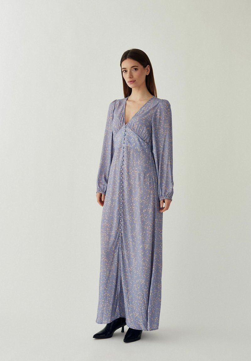 Femme portant une robe maxi à manches longues lavande avec de petits imprimés floraux et un devant à boutons, assortie à des bottines à talons noires.