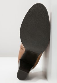 Semelle d'une chaussure en cuir marron avec un dessous noir texturé et un talon bas reposant sur une surface blanche.