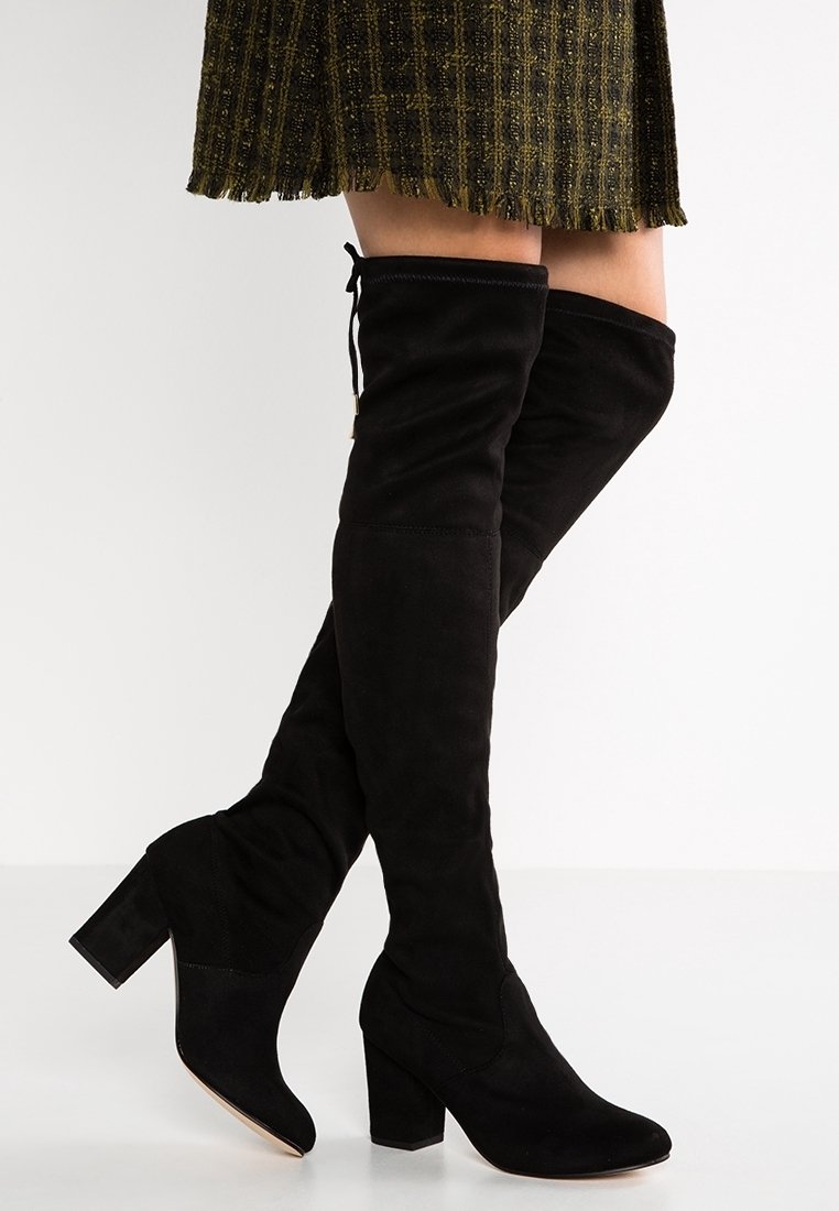 Bottes en daim noires montant jusqu'au genou, avec un bout arrondi et un talon bloc. Elles présentent une texture lisse et un design chic avec un style sans fermeture, à enfiler.