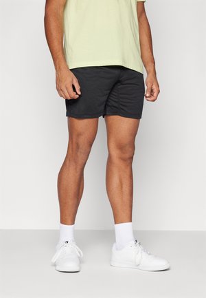 Shorts atletici neri con un motivo testurizzato, abbinati a una maglietta verde chiaro e scarpe da ginnastica bianche, indossati da una persona in piedi.