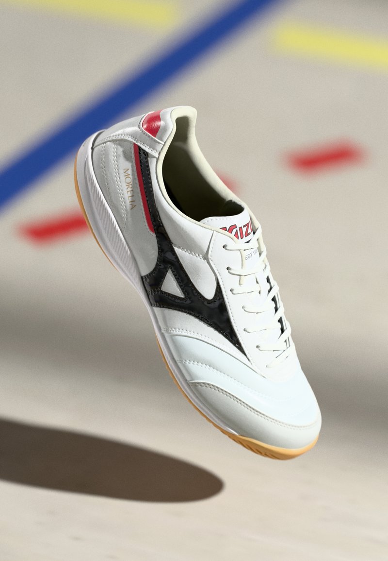Witte binnensport schoenen met een zwart driehoekdesign, rubberen zool en rode accenten. Beschikt over een gestructureerde bovenkant met veters en branding.