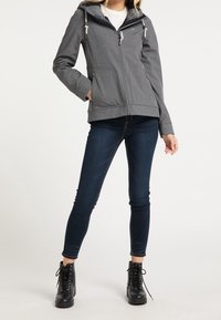 Grå zip-up jacka med huva, utrustad med två framfickor, justerbara dragskoar och en slät textur, kombinerad med mörka jeans och svarta stövlar.