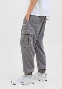 Graue Cargohosen mit elastischen Bündchen, Seitentaschen und einer aufgesetzten Tasche am Oberschenkel. Kombiniert mit weißen Sportschuhen.