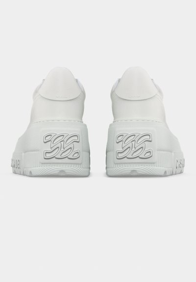 Ζευγάρι λευκών αθλητικών παπουτσιών που φαίνονται από πίσω, με υφασμένα πέλματα και ανάγλυφες σημάνσεις "SS" και "C.R.A.G.S.A.O.E.I" στο πλάι.