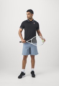 Svart polo skjorte med hvite striper, logo på brystet; lyseblå shorts; holder et tennisracket med en ball; svarte joggesko.