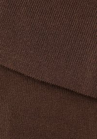 Detailný záber na zloženú hnedú rebrovanú pleteninu zobrazujúcu zvislé štruktúrované línie a mäkké tkanie materiálu.