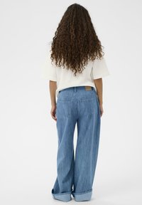 Široke denim hlače svetlo modre barve z rahlo zbledelim zaključkom. Imajo dve zadnji žep in zvit rob. Material se zdi mehak.