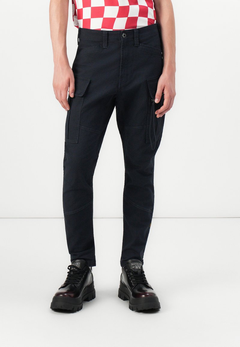 Dark navy cargo pants with a tapered fit, featuring multiple side pockets and stitched accents. Material appears durable with a smooth texture.