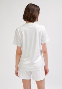 Biała sportowa koszulka z krótkim rękawem, wykonana z gładkiej tkaniny, o prostym wzorze bez widocznych zdobień czy logo.