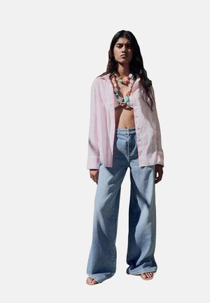 Rosa och vita randig oversized skjorta, ljusblå vida jeans och ett flerfärgat pärlhalsband. Avslappnad, löst sittande stil.