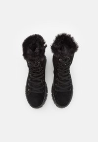 Paire de bottes montantes noires avec des semelles épaisses en caoutchouc, des lacets noirs, et une bordure en fourrure duveteuse autour des ouvertures des chevilles.