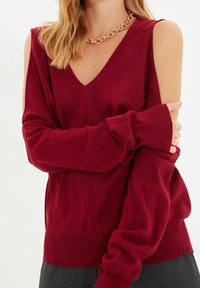 Bordowy sweter z dekoltem w serek i odkrytymi ramionami. Miękka dzianina, ściągacze na mankietach i dopasowany dół. Uzupełniony o masywny łańcuch na szyi.