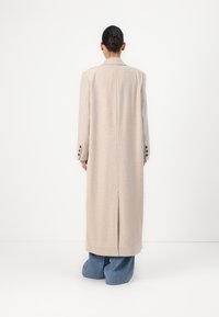Beige ribbed long coat with a notched collar, single vent at the back, and buttoned cuffs. Paired with wide-leg denim trousers.