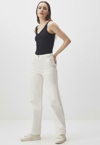 Pantaloni bianchi a gamba larga con tasche anteriori, zip, e dettagli di cucitura sottili, abbinati a un top fitted nero e sneakers bianche.