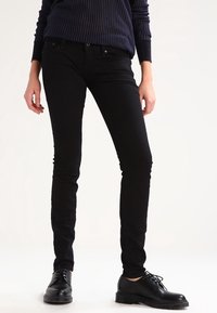 Svarta slim-fit jeans med en slät yta, fem fickor och metalldetaljer. Matchas med svarta snörskor och en marinblå ruggad tröja.