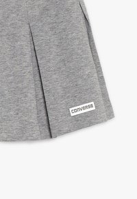 Šedá jersey sukně s sklady, na dolním lemu má bílou nášivku s logem Converse. Jednoduchý design a hladká textura.