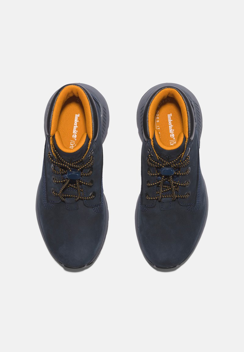Granatowe zamszowe buty z żółtymi wkładkami, z okrągłymi sznurowadłami i teksturowaną gumową podeszwą. Akcentowane przeszycia podkreślają design.