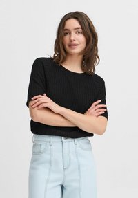 Sort ribbet striktop med korte ærmer og rund halsudskæring, kombineret med lyseblå højtaljede denimjeans.