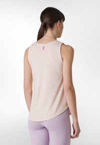Ljusrosa ärmlös topp med rund halsringning och böjd nederkant. Har en liten rosa etikett på baksidan. Tyget verkar mjukt och ventilerande.