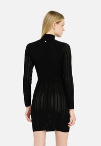 Robe noire à manches longues avec une texture tricotée à motifs, dotée d'un col haut et d'un accent argenté au niveau de la nuque. Silhouette cintrée.