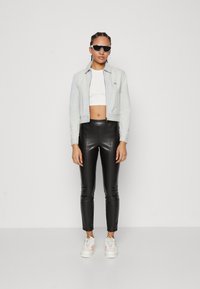 Světle modrý zkrácený kabát, bílý crop top, černé kalhoty z umělé kůže a bílé tenisky s růžovými akcenty. Modelka nosí tmavé sluneční brýle.