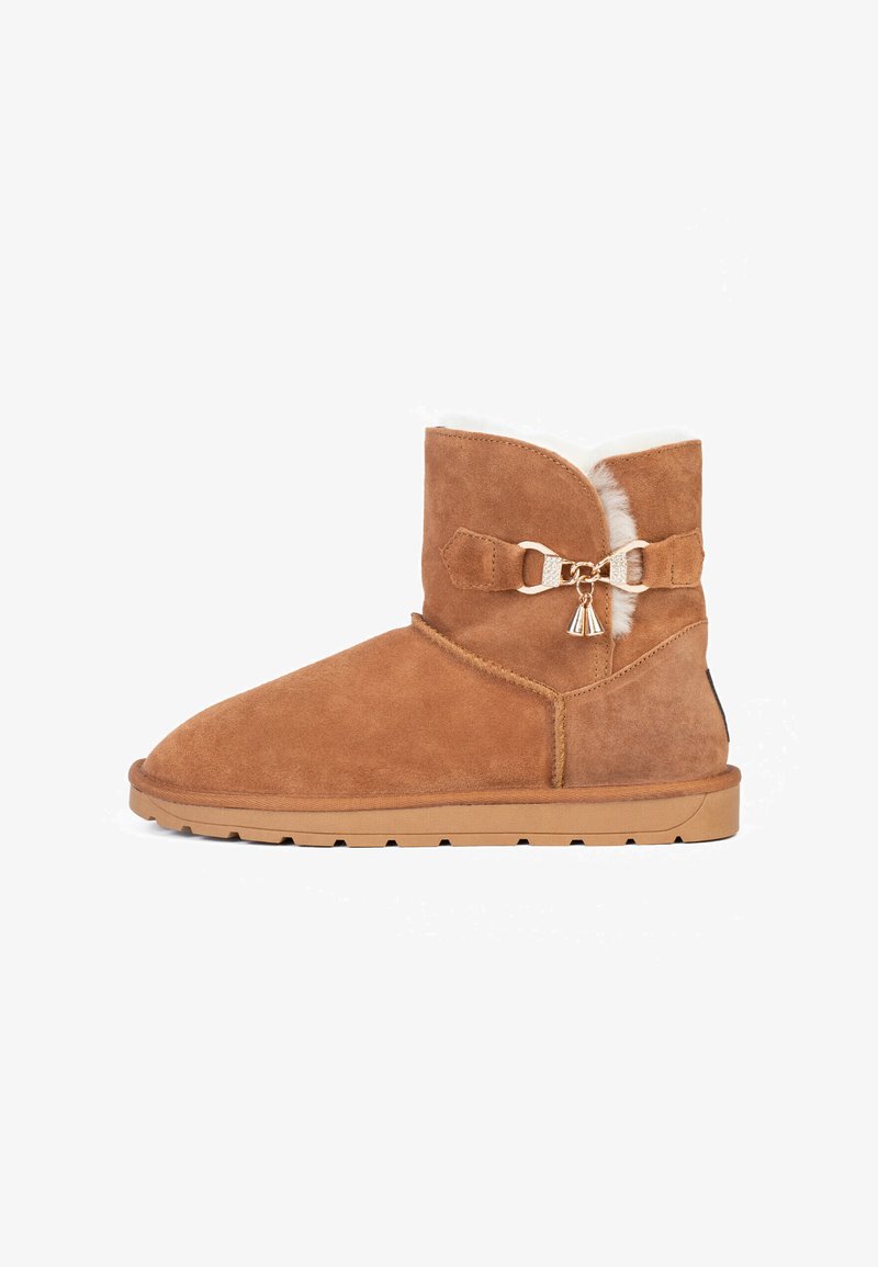 Botín corto de ante en tono marrón claro, con puntera redondeada, forro de piel sintética, lazo decorativo y acento metálico, y suela de goma con dibujo.