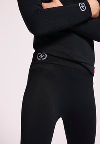 Set atletico nero composto da un top a maniche lunghe testurizzato con maniche a motivo e leggings aderenti. Entrambi i pezzi presentano sottili accenti con logo.