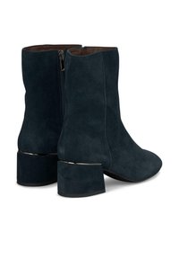 Botines de ante azul oscuro con tacón rectangular, cremallera lateral y textura suave, con un acento metálico en la base del tacón.