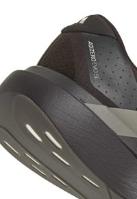 Μαύρο αθλητικό παπούτσι με υφή στη πάνω επιφάνεια, αφρώδη ενδιάμεση σόλα και μοτίβο στην εξωτερική σόλα. Διαθέτει έντονο λογότυπο και ανοίγματα για εξαερισμό.