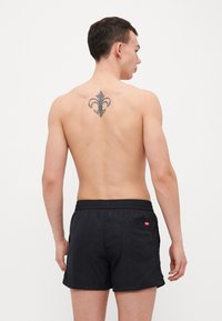 Shorts de bain noirs en tissu léger, dotés d'une taille élastique et d'une poche arrière. Présentés avec un tatouage dans le dos.