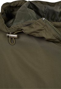 Olivgrön jacka med en lätt, slät textur. Har en dragkedja framtill, justerbar dragsko i huvan och kontrasterande foder.