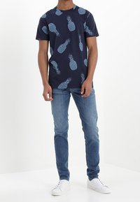 Camiseta de algodón azul marino con un patrón de piñas en azul claro, combinada con vaqueros azul claro y zapatillas blancas.