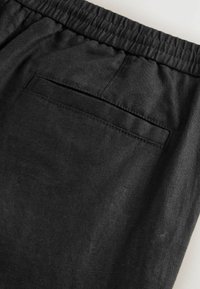 Pantaloni negri din in cu un brâu elastic, textură moale și un singur buzunar pe spate cu detalii cusute.