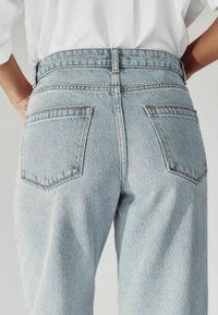 Gaiši zili augstās jostas bikses ar divām aizmugurējām kabatām, teksturētu džinsa apdari un kontrastējošiem šuvēm gar malām un kabatām.