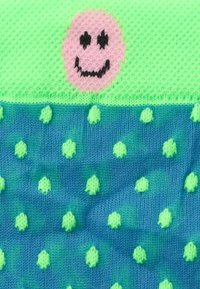 Zöld tetejű kötött zokni, melyen rózsaszín mosolygós arc látható, és kék alja apró zöld pöttyökkel, puha fonalból készült.