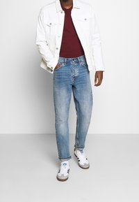 Vit denimjacka, vinröd tröja, ljusblå tapered jeans och grå sneakers med svarta och vita detaljer. Enkel, avslappnad outfit.