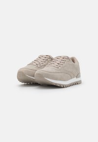 Light beige athletic shoes with textured fabric, lace-up design, thick white midsole, and serrated outsole for traction.