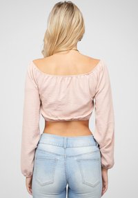 Top corto a maniche lunghe, in rosa chiaro, con scollo all'americana e lavorazione all'uncinetto sul retro, abbinato a jeans di denim blu chiaro a vita alta, che mostrano una texture liscia.