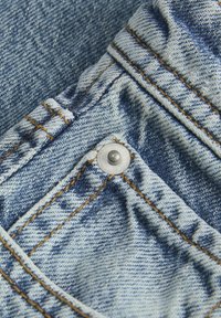 Light blue denim fabric with visible stitching and a metallic rivet. The texture shows some fading and creasing details.