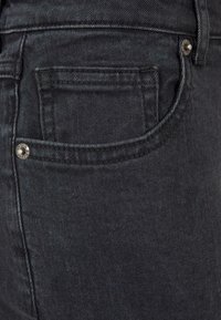 Tejido de mezclilla negra con una textura suave, que cuenta con un bolsillo trasero, herrajes plateados y costuras planas para mayor durabilidad.