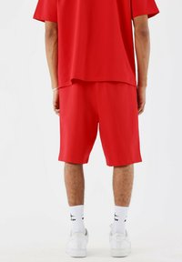 Rode kortearmige shirt en bijpassende shorts. De stof is glad en heeft een relaxte pasvorm. Draagt zich met witte sneakers en sokken.