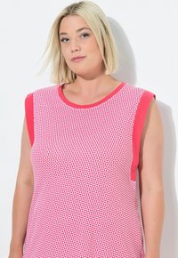 Top sin mangas de color rosa con un patrón geométrico blanco, escote redondo, y acentos en los hombros de color rosa sólido. Textura de tela suave.