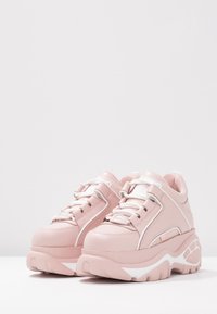 Chunkiga rosa sneakers med en slät yta, vita detaljer, ett traditionellt snörningssystem och en tjock, vit sula med konturdetaljer.