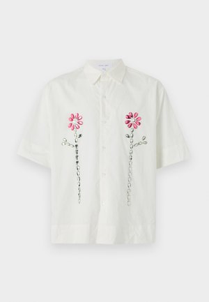 Bela kratka majica s kratkimi rokavi in ovratnikom, ki vključuje rožnate vezenine cvetlic in zeleni poudarek na sprednji strani. Oblikovanje z gumbi, lahka tkanina.