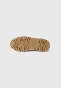 Semelle de bottes en caoutchouc brun avec de profondes rainures et un motif d'ergots. Caractéristiques d'un design plat et large pour la stabilité et l'adhérence sur diverses surfaces.