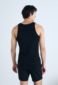 Schwarzes Tanktop aus Baumwolle, mit klassischem Schnitt, weiten Armausschnitten und rundem Ausschnitt, kombiniert mit schwarzen Shorts.
