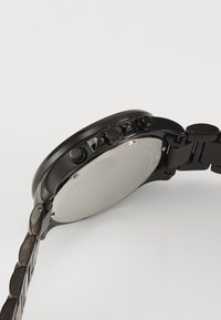 Montre-bracelet chronographe noire avec un boîtier rond, un bracelet texturé, plusieurs boutons de fonction et un dos lisse.